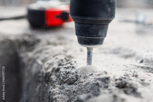 Drill bit boring into a rough, dusty concrete surface. Industrial action and creation of construction dust as powerful tool operates. Rotary hammer drill bit boring into a concrete or masonry surface