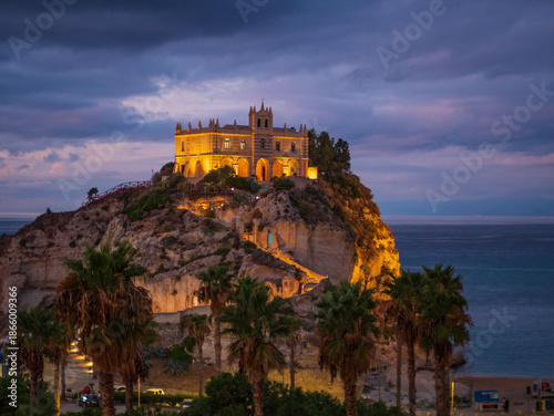 Tropea cliff sanctuary at dusk in Calabria, illuminated historic church on rocky promontory above Tyrrhenian Sea, dramatic clouds, coastal landmark, southern Italy travel destination