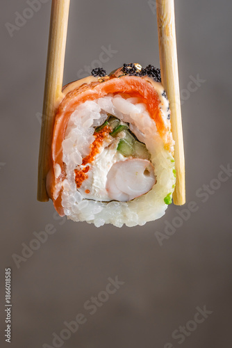Sushi roll held with chopsticks close up isolated on neutral background