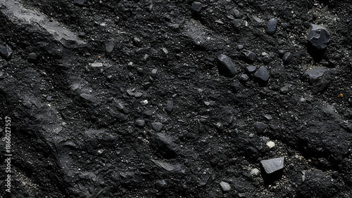 Close-up view of rough dark granular surface with scattered black rock fragments
