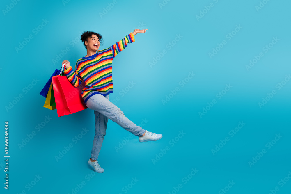 Obraz premium Young woman with colorful striped sweater joyfully shopping against blue background