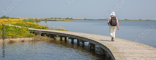Walking on the boardwalk at Marker Wadden in the Netherlands during a sunny day with flowers and water nearby