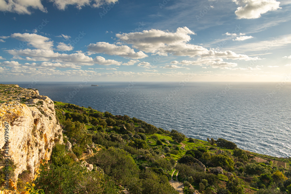 Naklejka premium Golden hour sunset at the rugged Dingli Cliffs in Malta, with warm light illuminating the rocky terrain and small clouds over the Mediterranean Sea.