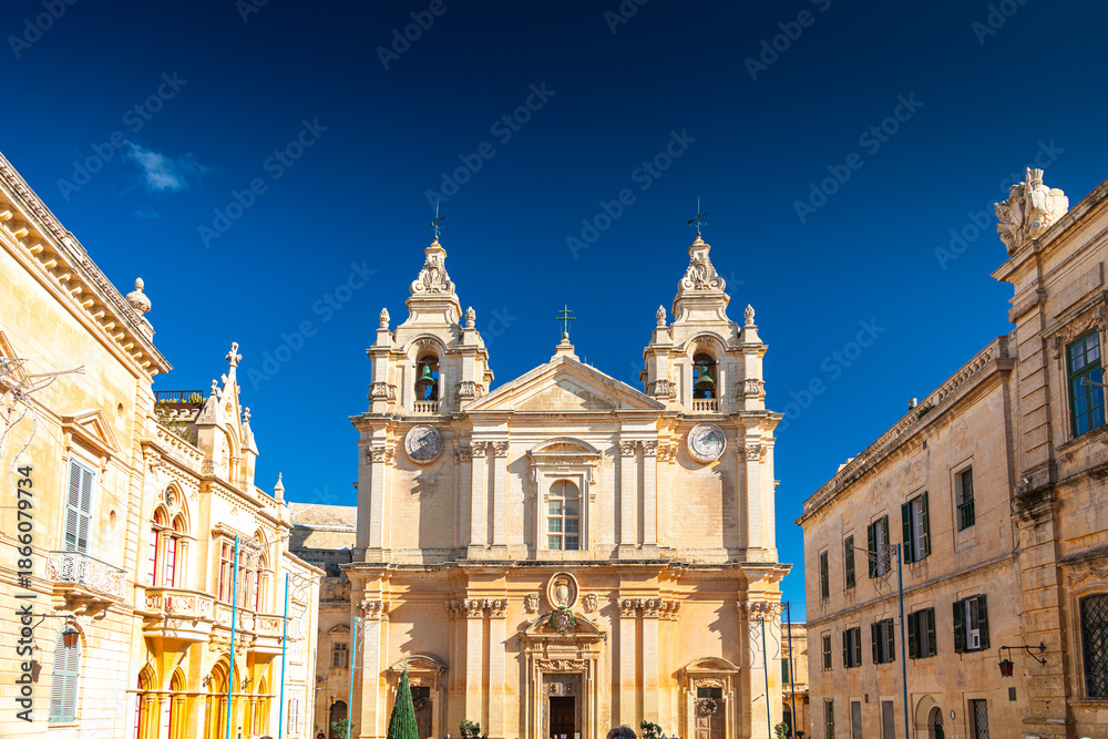 Fototapeta premium Church of Mdina, Rabat. Detailed view of a baroque church bell tower behind a limestone building in the historic city of Mdina, Malta. Travel to Malta. Mdina Cathedral.