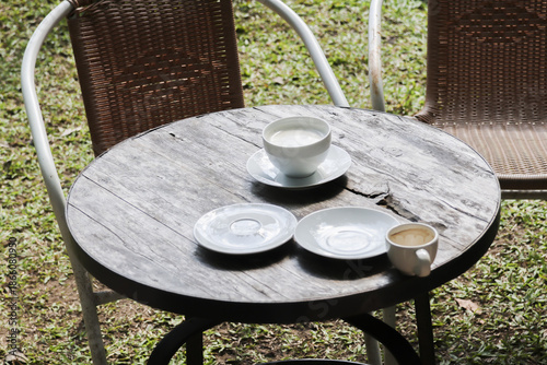 Relaxing outdoor wooden table scene with white ceramic cup of hot coffee and saucer offering peaceful morning atmosphere in green garden park for calm breakfast break time
