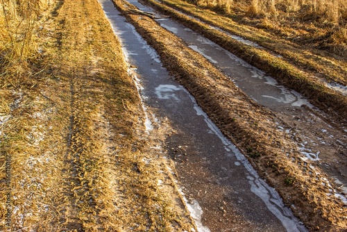 Foto Deep, muddy tire ruts on a rural dirt road covered by thin winter ice