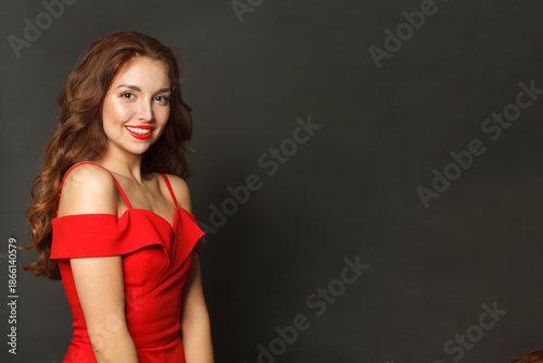 Studio portrait of fashion model woman with shiny skin, wavy hairstyle and red lips makeup on black background