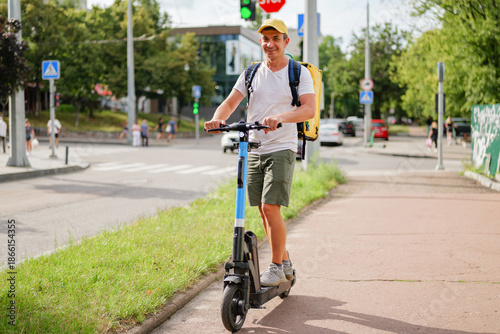 Wallpaper Mural Man moves on an electric scooter down a city street with traffic and pedestrians. It is a sunny day and he carries a backpack Torontodigital.ca