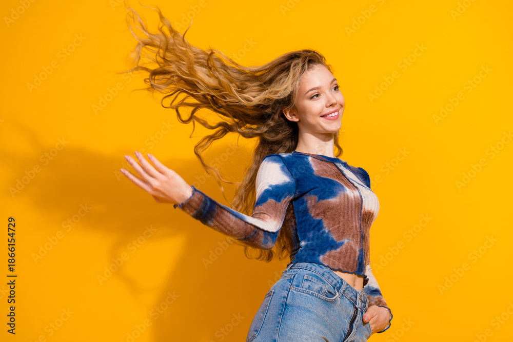 Fototapeta premium Young woman with flowing hair in tie dye top poses against bright yellow background showcasing casual style and confident joyful energy
