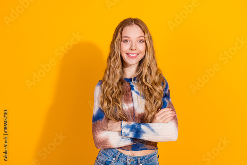 Young woman with long blonde hair wearing tie dye top and jeans stands against a bright yellow background smiling for a fashion lifestyle image