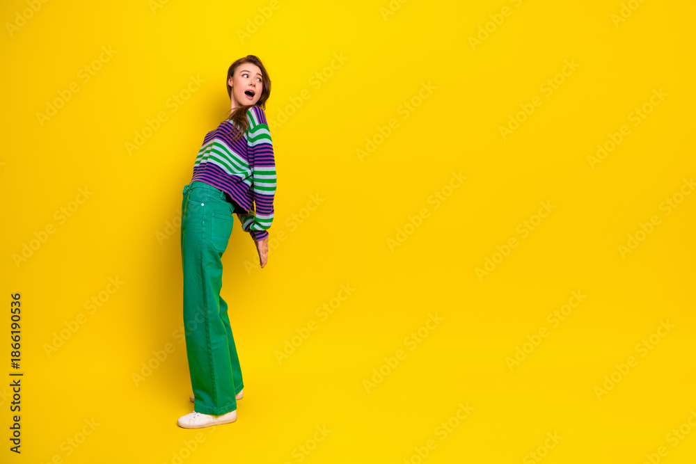 Fototapeta premium Young woman in striped sweater and green jeans poses joyfully against a bright yellow background