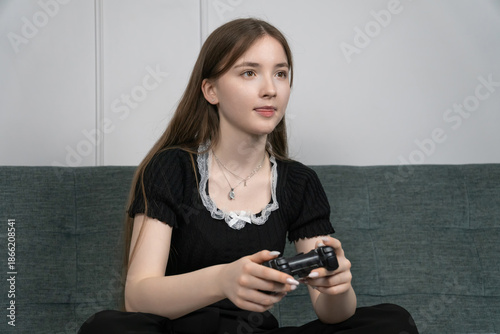 Concentrated teenage girl playing video games on a cozy sofa at home, gripping a joystick while focusing intently on the screen, immersed in her gaming experience