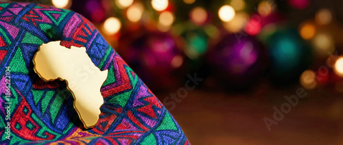 Golden Africa map pendant on colorful patterned fabric. Festive bokeh background with copy space. African Afrodescendant Culture Day concept