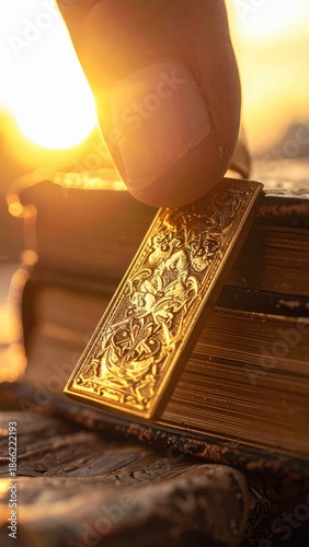 Close up of finger holding antique golden bookmark with detailed engraving against sunlit old book outdoors