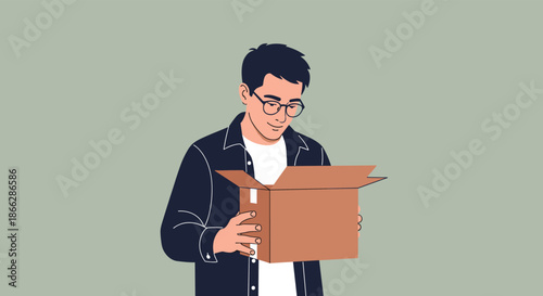 A happy young man wearing glasses and a dark jacket smiling as he looks inside an open cardboard box he is holding.