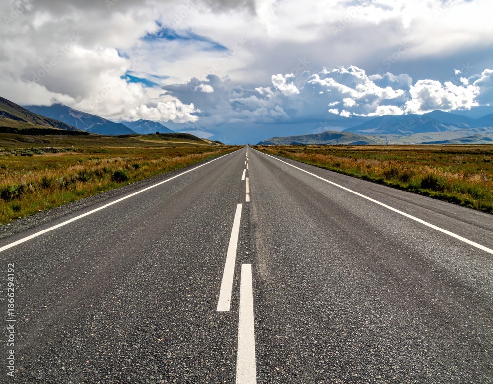 Fototapeta premium Asphalt road stretching towards mountains under dramatic cloudy sky