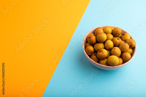 Ripe Longan in ceramic bowl on blue and orange pastel paper, side view, copy space
