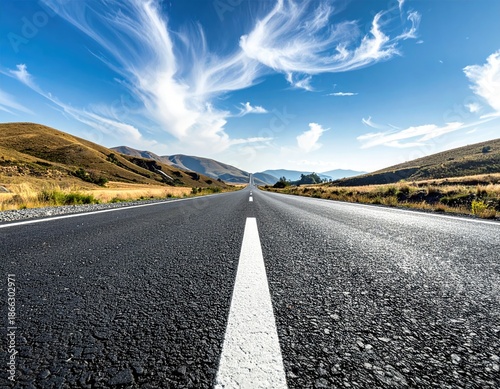 Road vanishing toward distant hills under a wispy, bright blue sky