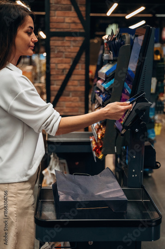 Принти на полотні Young woman using self-checkout kiosk in a modern grocery store, showcasing tech