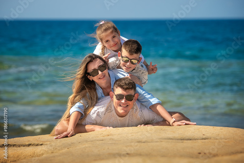Φωτογραφία A joyful family of four has fun building a human pyramid on coastal sandstone rocks against the backdrop of the blue sea