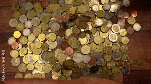Top-down view of female hands gathering, lifting, and dropping a pile of euro coins on a wooden table, symbolizing wealth and savings