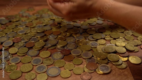 Woman's hands playing and counting a pile of euro coins on a wooden table. A concept of richness, greed, earnings, and savings