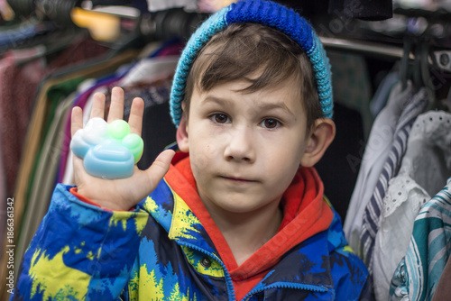 Close-up portrait of a little boy holding a bright paw-shaped fidget toy on his palm.