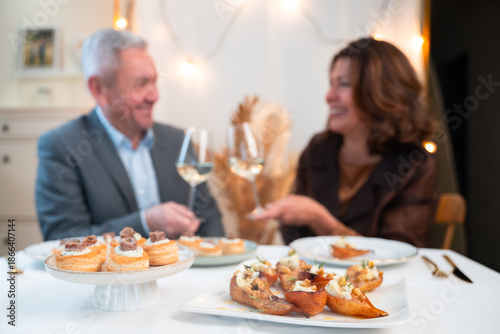 Gourmet appetizers in foreground with mature couple toasting white wine during an elegant home dinner