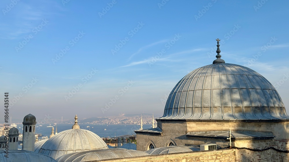 Fototapeta premium Daytime aerial view of the Süleymaniye Mosque lead-covered domes and the Istanbul skyline. Modern skyscrapers contrast with historic Ottoman architecture under a blue sky
