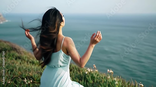 Young woman stands on a cliff overlooking the ocean, embracing the tranquility and freedom