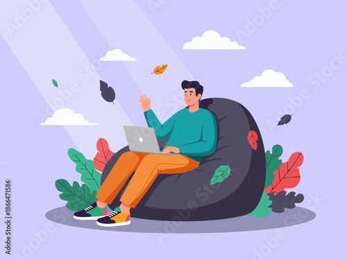 Man sitting on a gray bean bag chair working on laptop with leaves and flowers around him