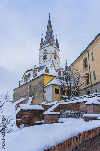 view of frozen downhill street with snow on roofs and main tower on top on cloudy winter day white landscape