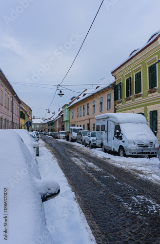 winter look of snowed cars on colorful street on old town transylvania 