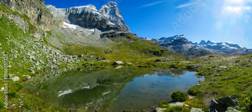 Matterhorn reflected in an alpine lake with clear water, rocky shoreline, and surrounding high altitude terrain in Switzerland. Mountain landscape showing iconic peak, glacial environment, natural sym