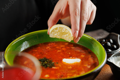 Fresh lemon slice added to a bowl of red borscht soup in a cozy dining setting