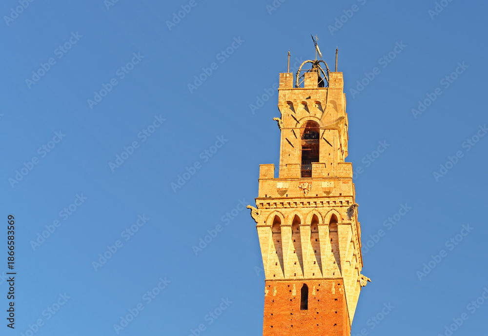 Fototapeta premium Famous bell tower 'Torre del Mangia' on the Piazza del Campo in the evening sun on a bright october day with blue sky in Siena, Tuscany