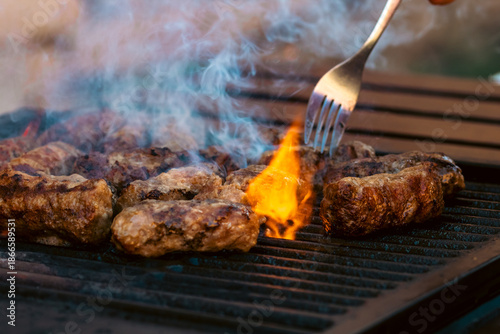 Preparing traditional Romanian meat rolls called mici or mititei on a hot barbecue grill with fire flames