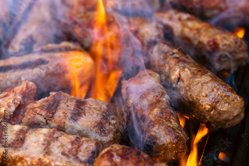 Preparing traditional Romanian meat rolls called mici or mititei on a hot barbecue grill with fire flames