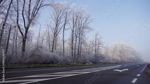 Empty road through frozen forest with frost covered trees at sunrise, 4K