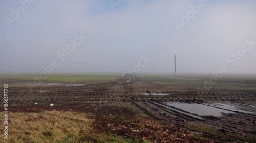 Muddy dirt road with tractor tire tracks in foggy field, 4K