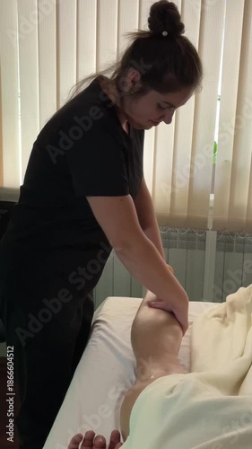 Female therapist applying oil and performing abdominal and leg massage on a client during therapeutic session