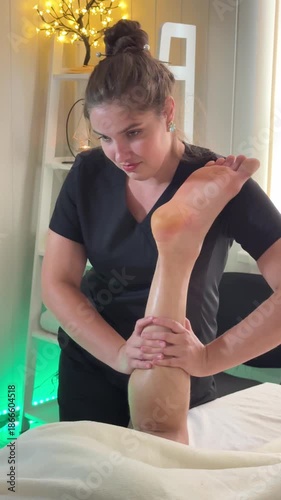 Massage therapist performing deep leg manipulation techniques on male client’s extended leg during session
