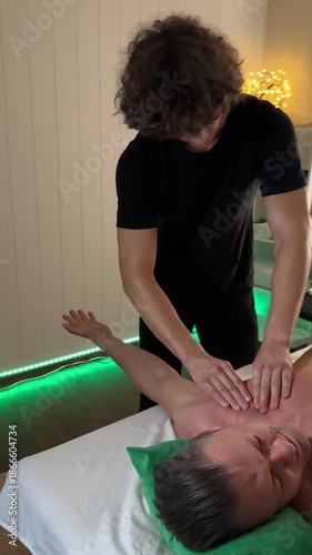 Chest massage with focused hand pressure performed by male therapist in spa with green ambient light