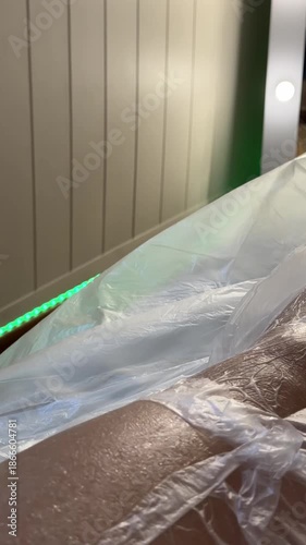 Close-up of a body covered in plastic wrap during a cosmetic wrapping procedure at a beauty salon