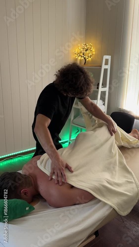 Therapist in black performing back massage using wrapped hand grip over client lying on massage table with towel