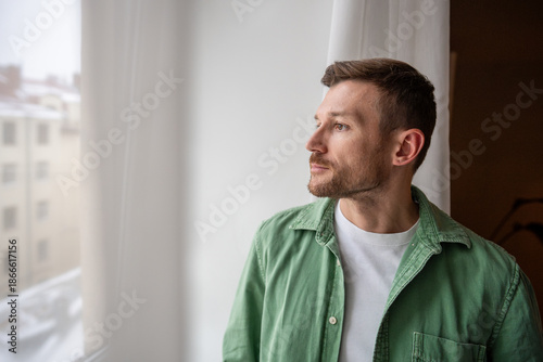 Φωτογραφία Thoughtful bearded handsome man with focused tranquil expression calmly looking at window, engaged in thinking process, brainstorming new work ideas, reflecting on life and finding inspiration