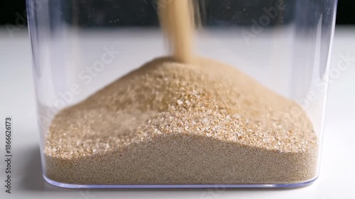 Pouring Light Brown Granules Into Clear Plastic Container With White Background