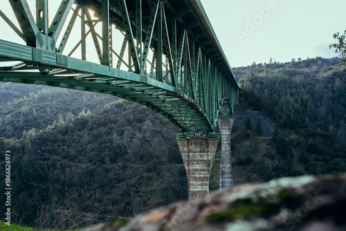 Tall green steel bridge with concrete supports above mountain valley