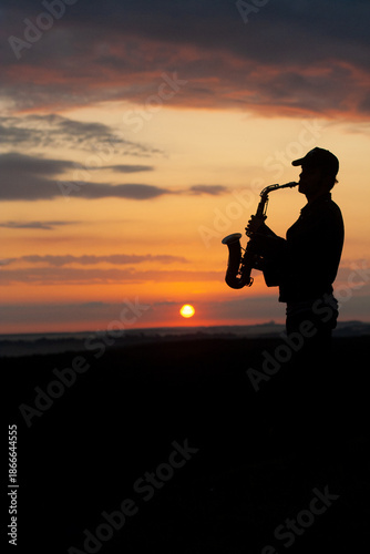 a boy musician plays the saxophone against the background of a beautiful sunset