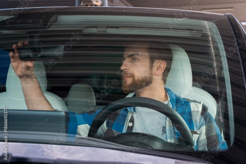 Photos Young bearded male looking in the rearview mirror of her car while getting ready for a trip